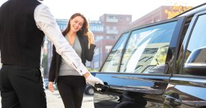 A professional driver opening the door to a black car. A woman smiles as she stands in front of the door.