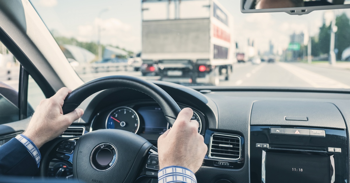 A close-up of a person gripping the steering wheel of a car with both hands while driving on a highway.